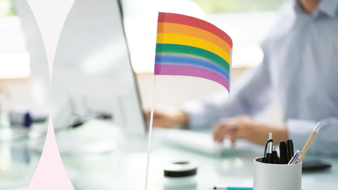 Mesa de escritório com bandeira do arco-íris, simbolizando orgulho LGBTQ+, em um ambiente de trabalho moderno e inclusivo.