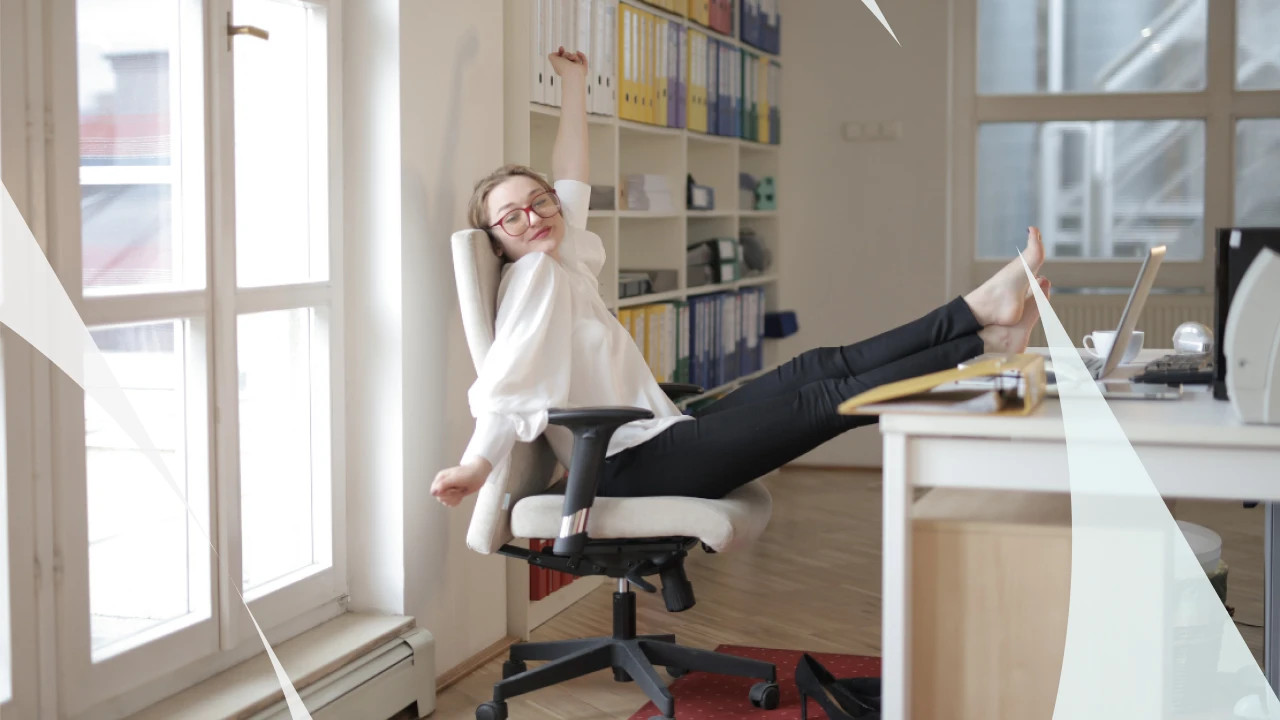 Mulher feliz e relaxada no escritório, sentada na cadeira com os pés elevados na mesa, cercada por livros e arquivos organizados, transmitindo bem-estar e satisfação no ambiente de trabalho.