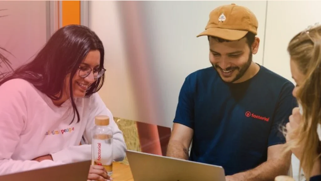 Grupo de jovens profissionais trabalhando e discutindo ideias em ambiente de coworking, colaborando e compartilhando conhecimento.