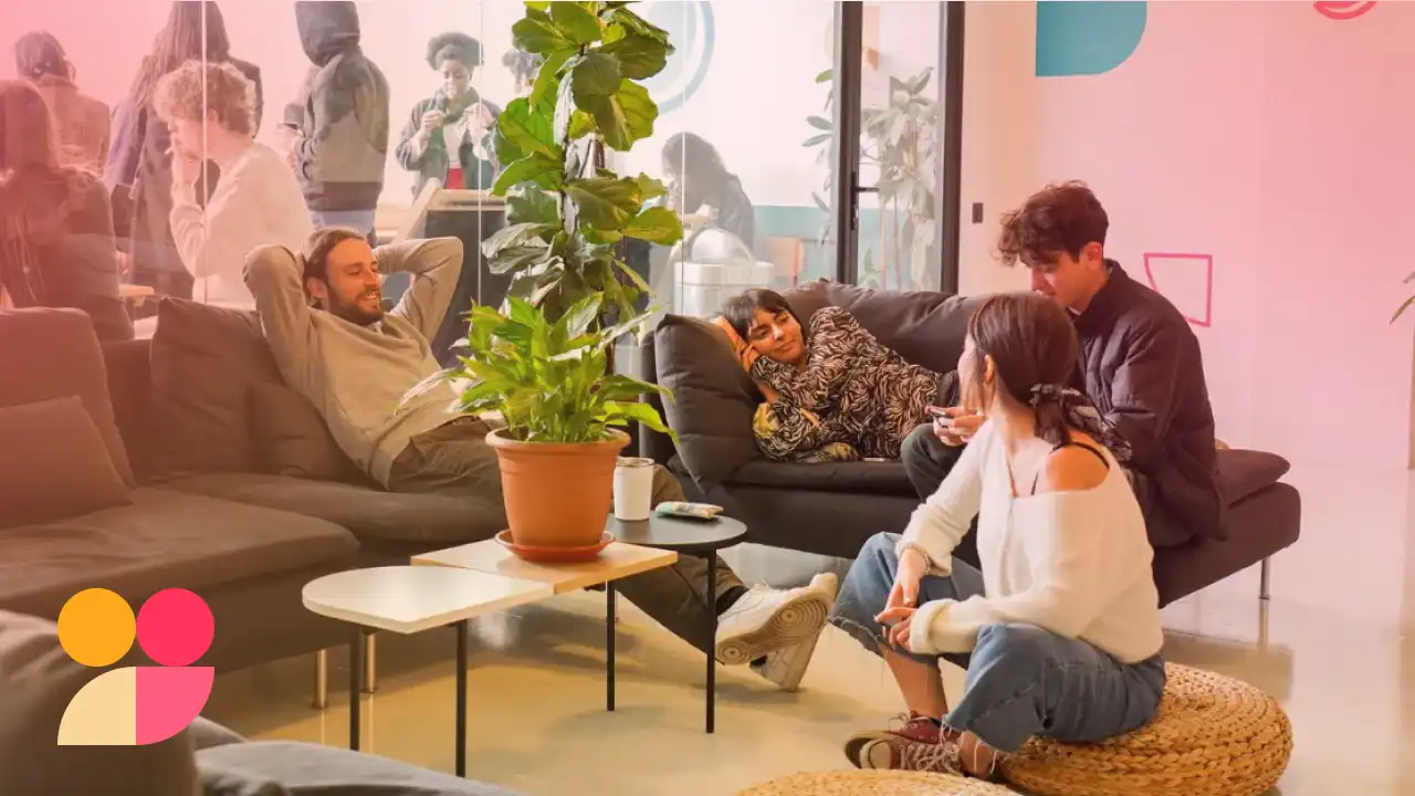 Grupo de pessoas descontraídas sentado em um sofá de sala, conversando e relaxando em um ambiente moderno e acolhedor.