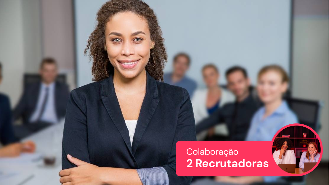 Mulher sorridente segurando documentos em frente ao computador, simbolizando colaboração e trabalho em equipe entre recrutadoras.